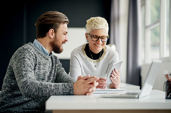A casually dressed male and female, seated looking at a tablet